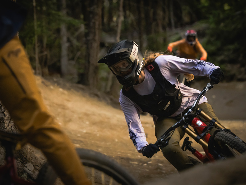 Mountain bikers descend a rugged alpine trail in Whistler Bike Park with sweeping mountain views in the background.