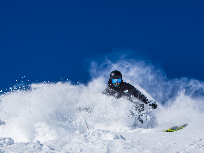 A certified ski guide carves through deep powder during a guided private backcountry skiing tour in Whistler's alpine terrain after fresh snowfall.