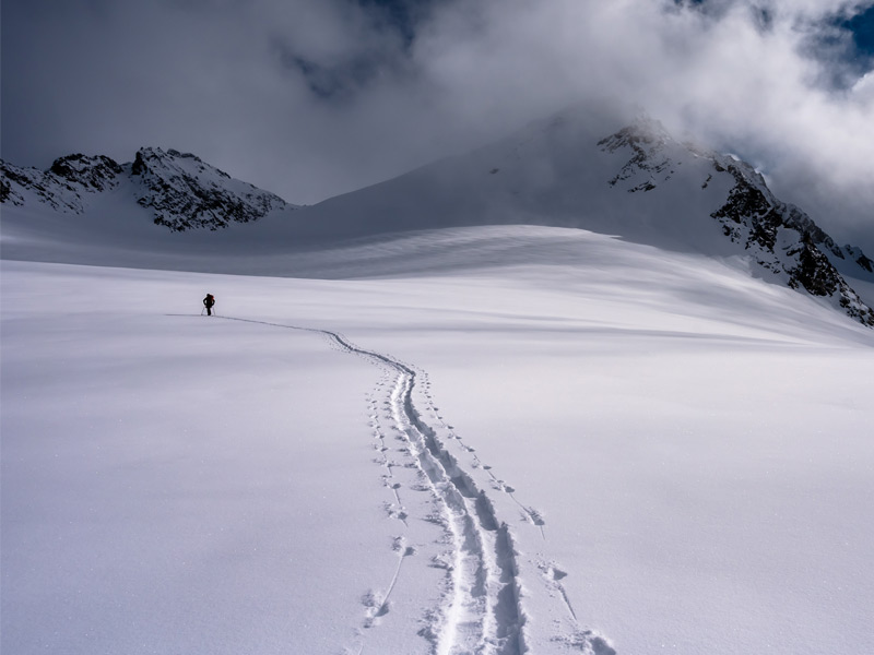 A skier follows fresh skin tracks across a remote alpine glacier during a private backcountry skiing tour in the Whistler backcountry.
