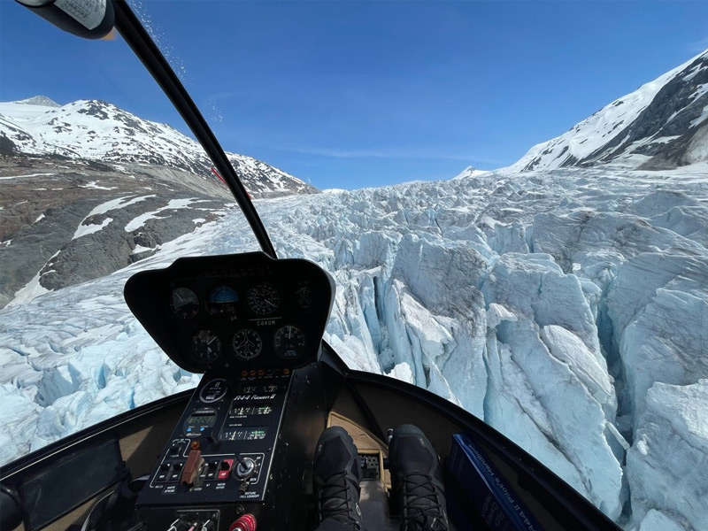 View from inside a helicopter cockpit flying above a dramatic glacier surrounded by snow-covered mountains on a Whistler alpine helicopter tour.
