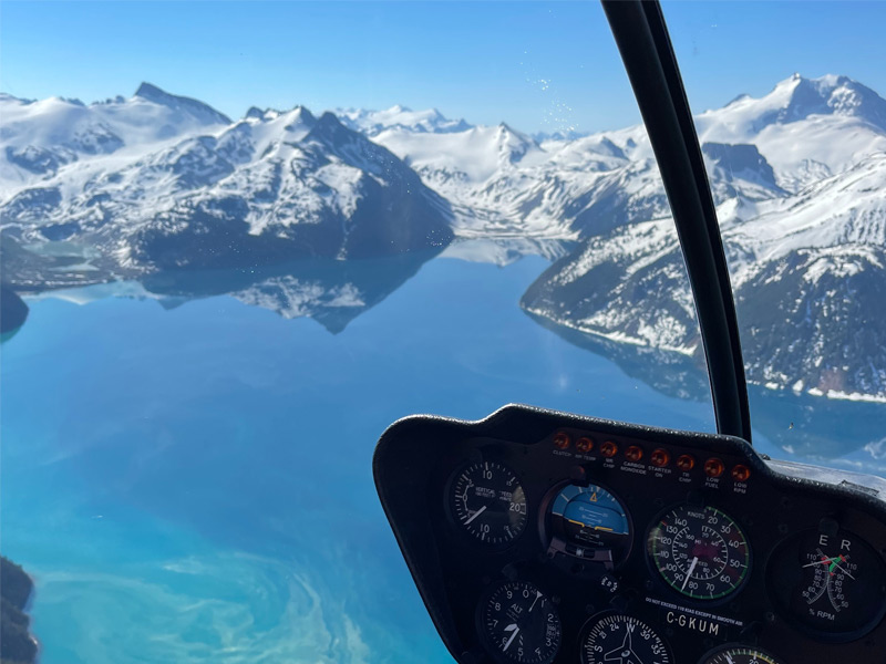 View from inside a helicopter above turquoise alpine waters and snow-covered peaks along the Sea to Sky corridor near Whistler.
