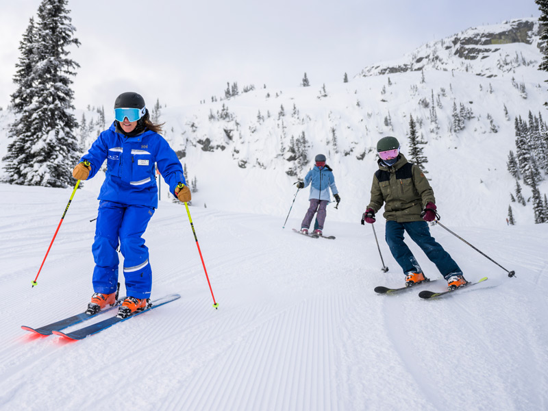 Four skiers gather with their skis on a snowy mountain overlooking the Coast Mountains in Whistler.