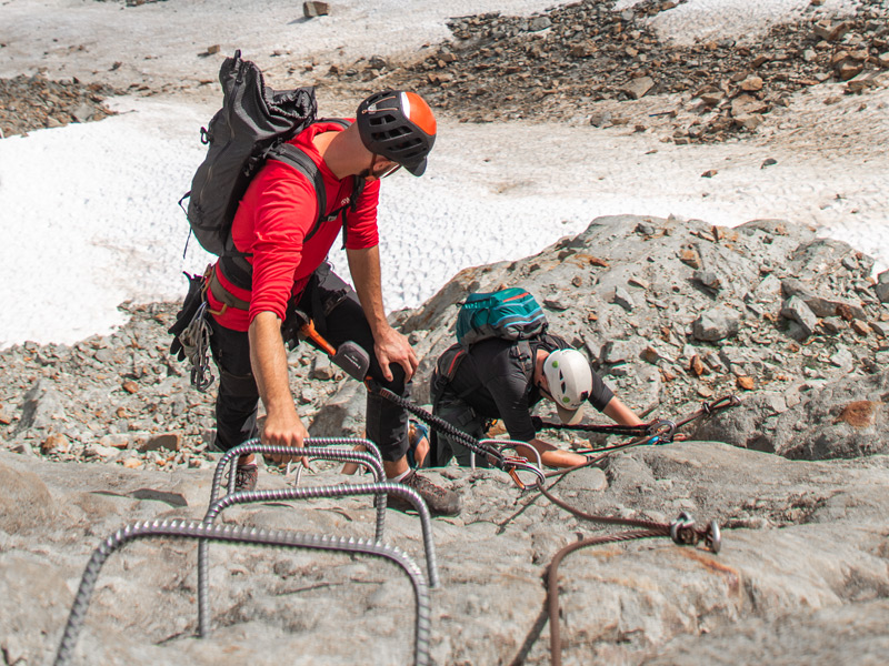 Via ferrata in Whistler, BC, two climbers clipped into safety cables climbing a steep rock face with metal rungs