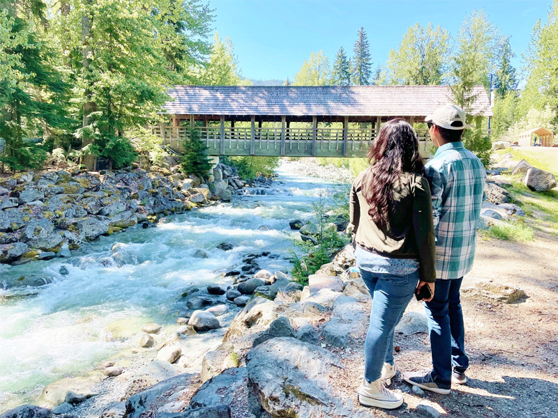 Two visitors on a walking tour beside Fitzsimmons Creek and the covered bridge in Whistler, BC.