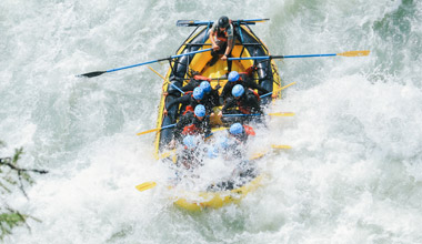 Group of rafters navigate a whitewater rapid in Whistler, paddling through crashing waves in an inflatable raft.