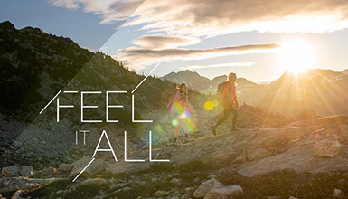 Two hikers trek across a rocky alpine ridge in Whistler as the sun sets behind jagged peaks, casting a golden glow over the landscape. 'Feel It All' captures the essence of adventure in the mountains.