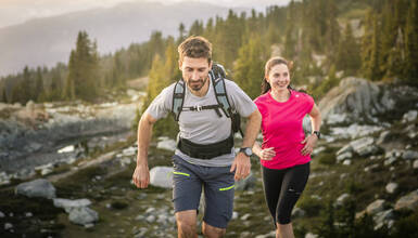 Trail runners enjoying a scenic alpine route in Whistler, surrounded by rugged terrain, trees, and mountain views during summer.