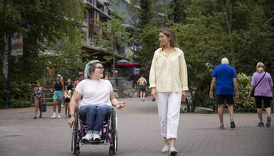 A person in a wheelchair rolling along the accessible Village Stroll beside another person on foot
