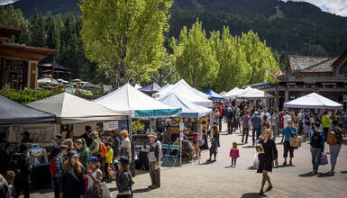 People shopping and eating at the Whistler Farmers' Market in the Upper Village on a sunny day.