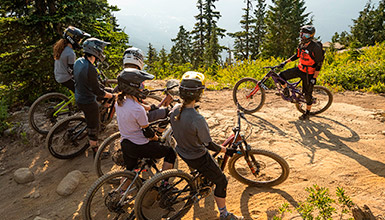Five people on mountain bikes getting instruction from a bike coach in the Whistler Mountain Bike Park
