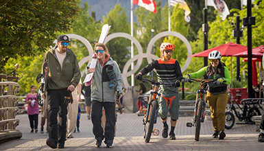 A group of people walking along Village Stroll with skis and bikes in springtime