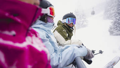 Three skiers on a snowy chaiflift at Whistler Blackcomb with a gondola cabin in the background