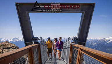 Three people walking across Cloudraker Skybridge at Whistler Blackcomb on a sunny, summer day