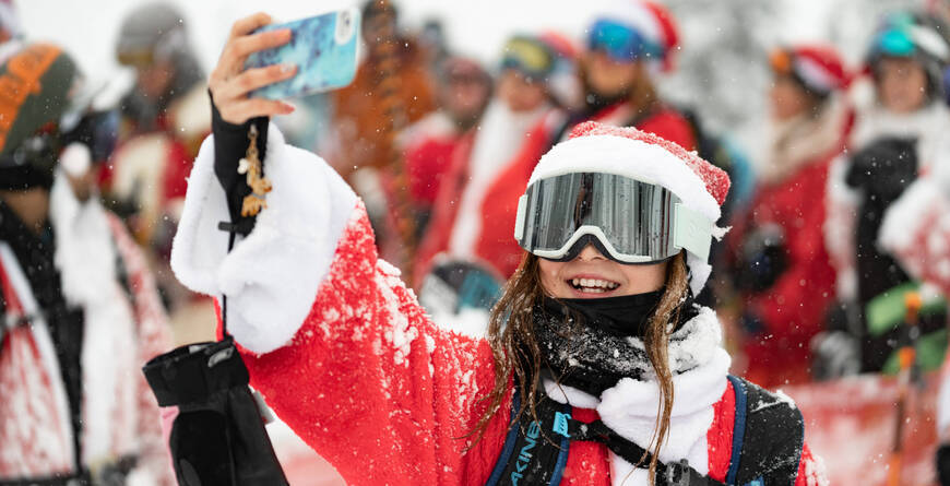 A person dressed as Santa taking a selfie in a crowd of other Santas