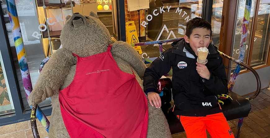 A child sitting next to a stuffed bear while eating ice cream in Whistler Village