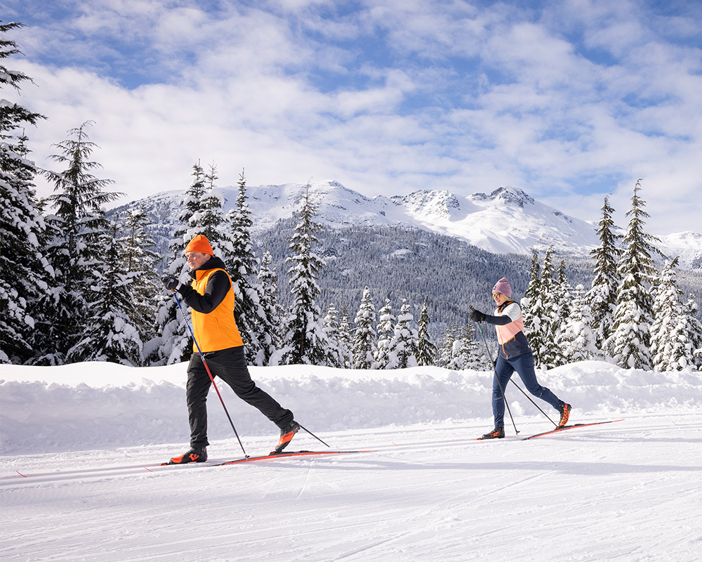 Cross-country skiers glide along snowy trail with Whistler Mountain views.